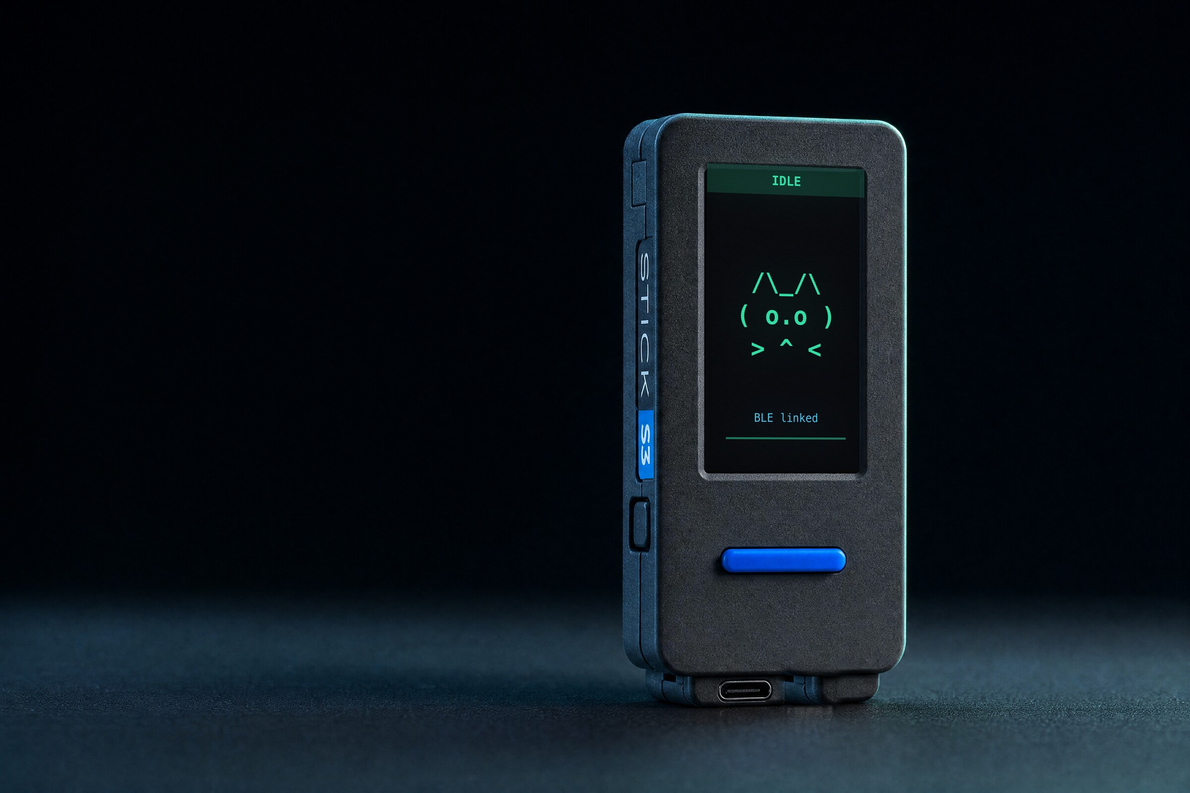 The Vibe Desktop Buddy device โ an M5StickS3 โ upright on a dark desk, its screen showing an idle ASCII pet and a live BLE link